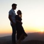 Couple on hilltop at sunset, man protective.
