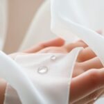 Sensory close-up, fabric, water, soft light, skin.